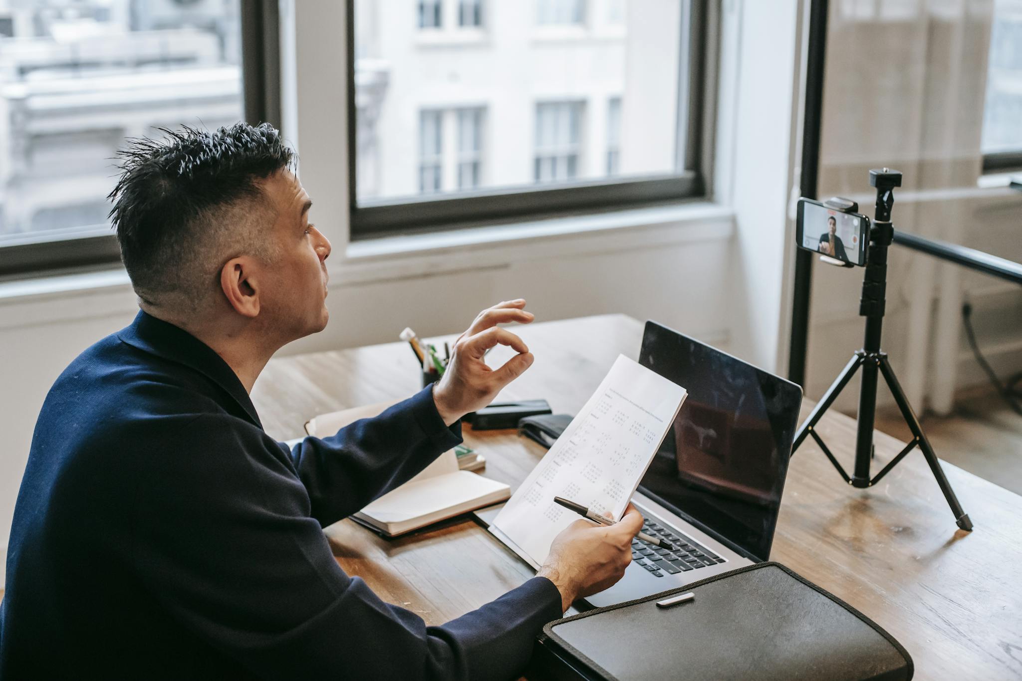 Man using laptop and smartphone for a video call in an office setting.
